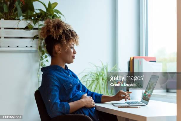 pregnant woman with hand on belly using laptop - pregnant stock pictures, royalty-free photos & images