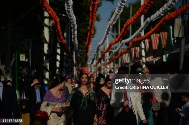 Women in traditional Sevillian dresses walk past "casetas" during the "Feria de Abril" festival in Seville on May 6, 2019. - The fair dates back to...