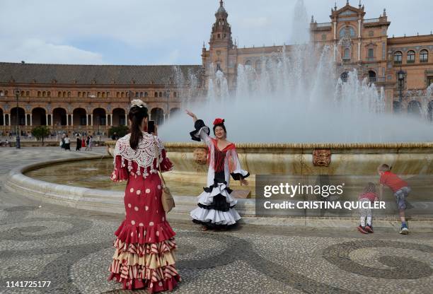 Tourists in traditional Sevillian dresses take photos at the Plaza de Espana square during the "Feria de Abril" festival in Seville on May 6, 2019. -...