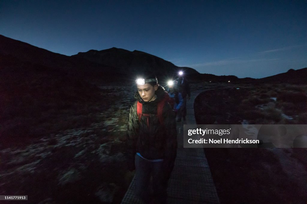 Family of three hikes in the darkness along a wooden boardwalk in Tongariro National Park