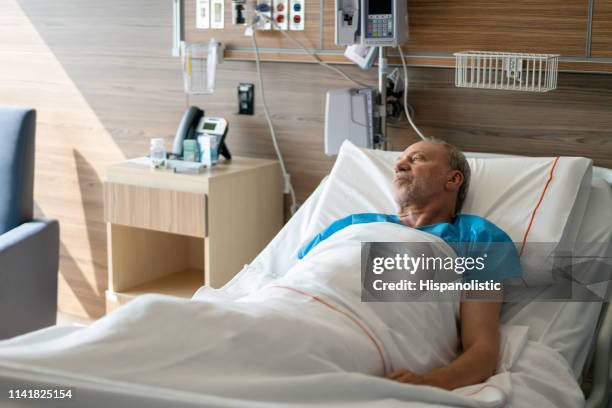 male latin american senior patient lying down on hospital bed looking away thoughtful - patient lying down stock pictures, royalty-free photos & images