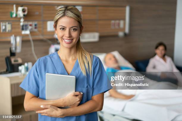 mooie verpleegster met een tablet geconfronteerd met camera glimlachend en senior patiënt liggend op bed op de achtergrond - woman smiling facing down stockfoto's en -beelden