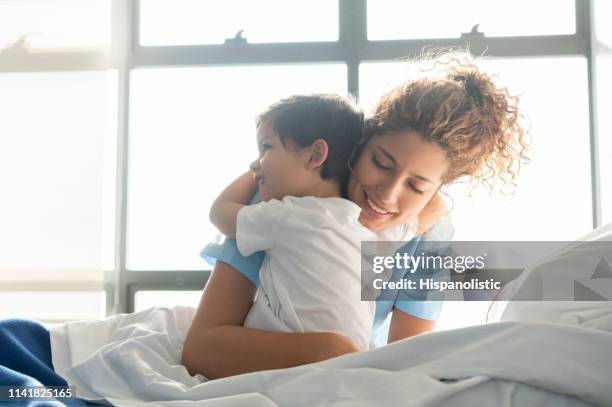 schöner süßer kleiner junge, der in der pädiatrie stationiert ist und junge krankenschwester umarmt - child in hospital stock-fotos und bilder