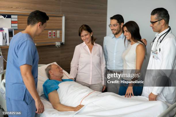 happy family visiting their dad at the hospital while nurse and doctor check senior patient - hospital visit stock pictures, royalty-free photos & images