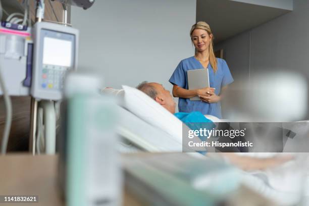 bellissimo residente medico che fa il giro controllando un paziente anziano mentre tiene in mano una compressa in ospedale - rapporto medico paziente foto e immagini stock