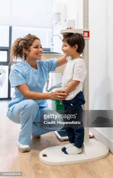 latijns-amerikaanse verpleegkundige het meten van een kindergeneeskunde patiënt controleren hos groei vooruitgang zowel glimlachend - nurse child stockfoto's en -beelden