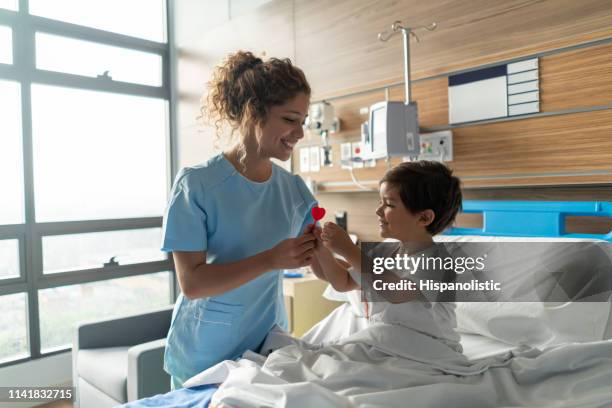 jonge mooie verpleegster het geven van een lollipop aan kindergeneeskunde ziekenhuis patiënt glimlachend - child hospital bed stockfoto's en -beelden