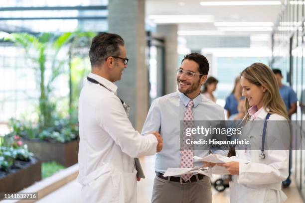 latin american hospital supervisor handshaking with male doctor at the hospital while holding some documents - team leader stock pictures, royalty-free photos & images