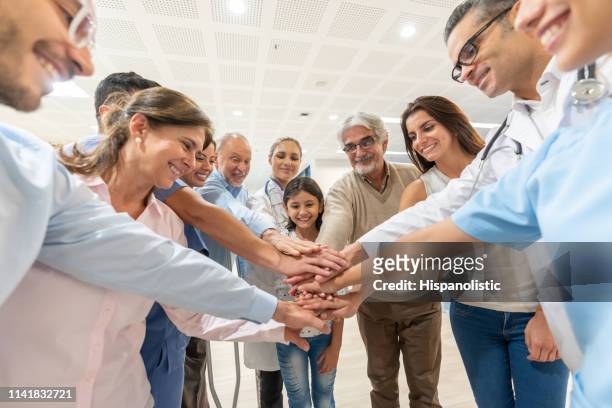 group of healthcare workers and patients of different ages in a huddle all with hands in smiling - team hands in huddle stock pictures, royalty-free photos & images