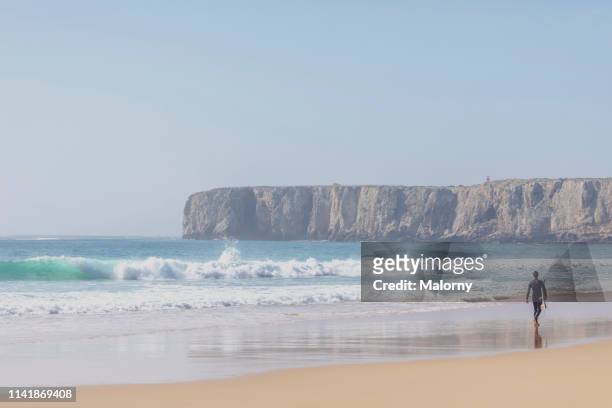 young man with surfboard on the beach, walking towards the wavy sea. - sagres ストックフォトと画像