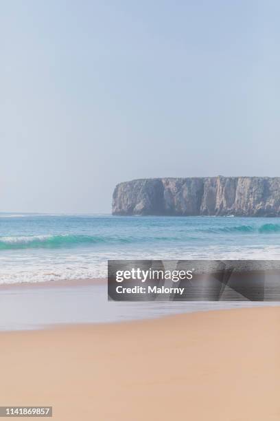 empty beach and wavy sea. rocky coastline in the background. - faro stock-fotos und bilder