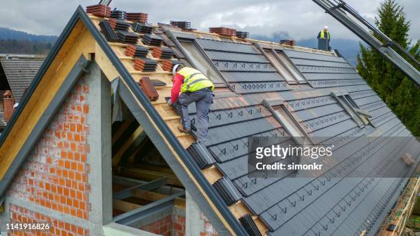 bauarbeiter arbeiten auf baustelle - house roof materials stock-fotos und bilder