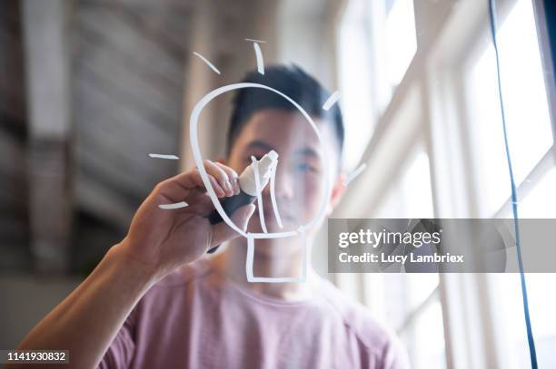 ideas! fifteen year old boy drawing a lightbulb on glass with a chalk marker - mening stockfoto's en -beelden