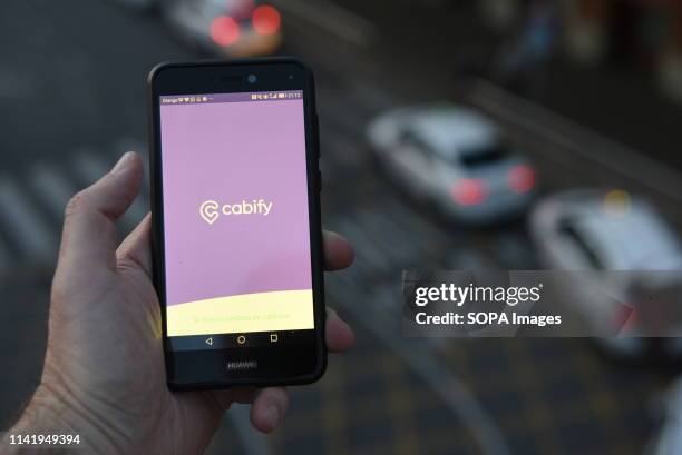 In this photo illustration a man seen holding a smartphone with the Cabify app outside Atocha train station in Madrid where taxi drivers usually wait...