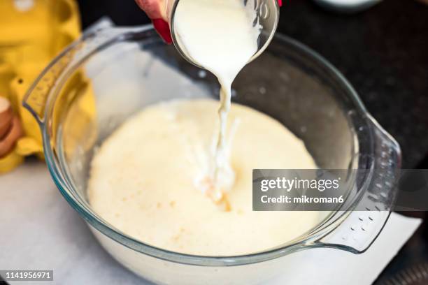 woman pouring milk into mixing bowl in kitchen. baking cake at home - bowl of sugar stockfoto's en -beelden