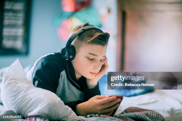 boy lying on bed listening to music through his wireless headphones - boy headphones imagens e fotografias de stock