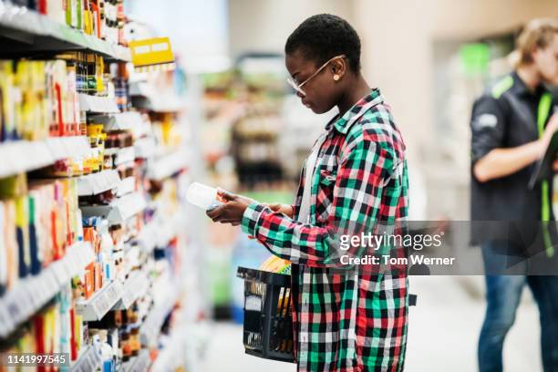 young woman reading label on food item in supermarket - shirt tag stock pictures, royalty-free photos & images