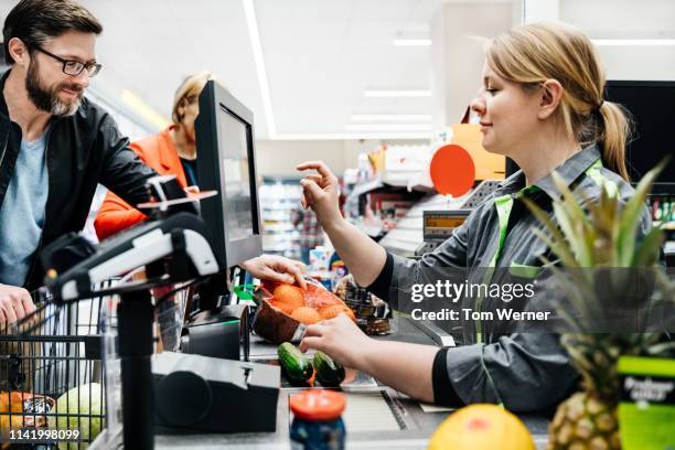 cashier ringing up mature couple's groceries bill - caissière stockfoto's en -beelden