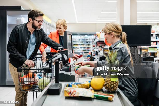 mature couple putting groceries on conveyor at checkout - ladenkasse stock-fotos und bilder