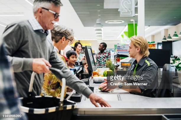 cashier ringing up senior couple's groceries - caissière stockfoto's en -beelden