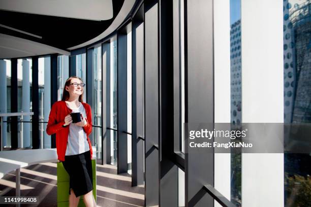 vrouw in het kantoor glimlachen in de zon in het raam koffie drinken - dag 1 stockfoto's en -beelden