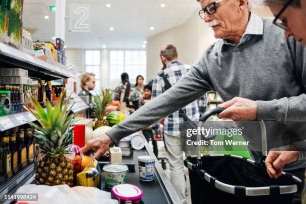 senior couple putting groceries on conveyor - checkout conveyor belt stock pictures, royalty-free photos & images