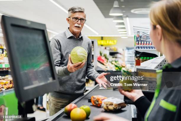 senior man holding melon and talking to cashier - caissière stockfoto's en -beelden
