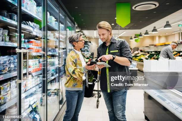 grocery store clerk assisting senior woman with query - assistant foto e immagini stock