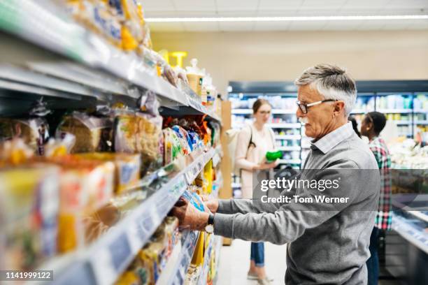 senior man picking out bread at supermarket - bread packet stock pictures, royalty-free photos & images