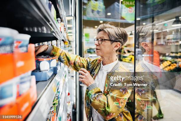senior woman picking groceries out of fridge - supermarket refrigeration stock pictures, royalty-free photos & images