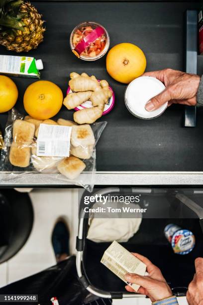 aerial view of senior couple placing groceries on checkout conveyor - cajero fotografías e imágenes de stock