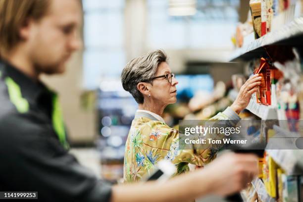 senior woman picking goods from shelf at supermarket - supermercado fotografías e imágenes de stock