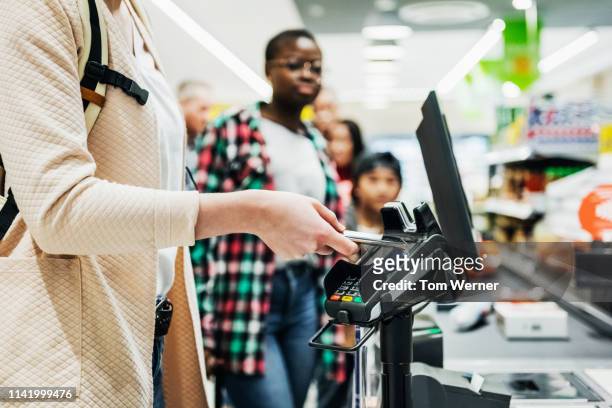 woman using smartphone to pay for groceries - card reader stockfoto's en -beelden