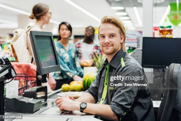 portrait of cashier sitting at checkout - kasse supermarkt stock-fotos und bilder