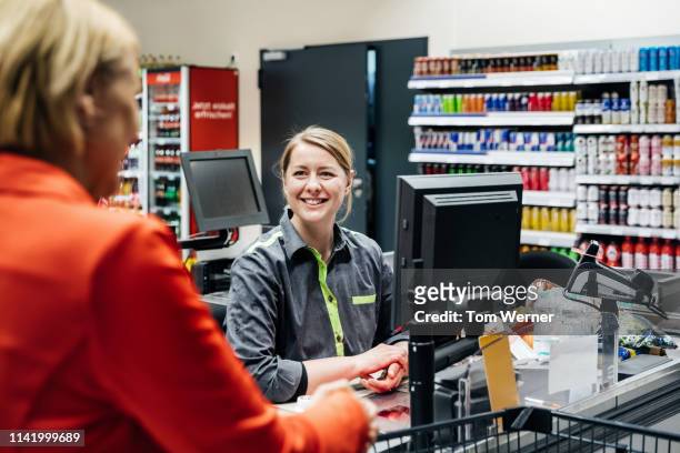 cashier smiling at customer buying groceries - caissière stockfoto's en -beelden