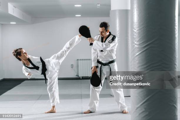 Caucasian handicapped highly motivated girl practicing taekwondo with her training. Girl kicking kick target.