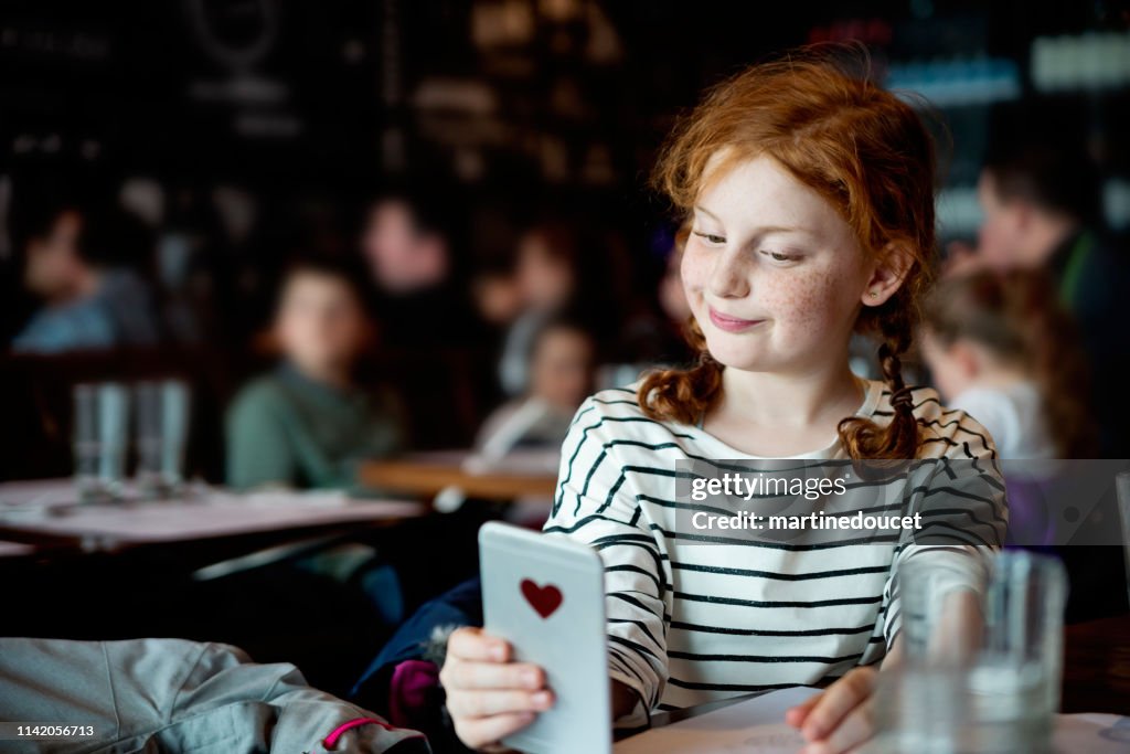 Chica preadolescente haciendo selfies en una mesa de restaurante.