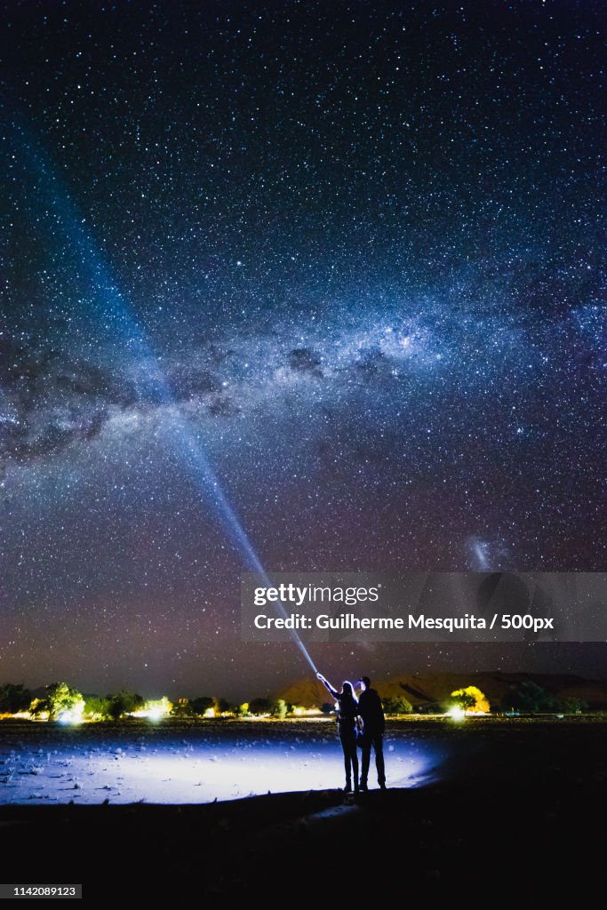 Couple With Flashlight Pointing To The Galaxy At The Sky Milky