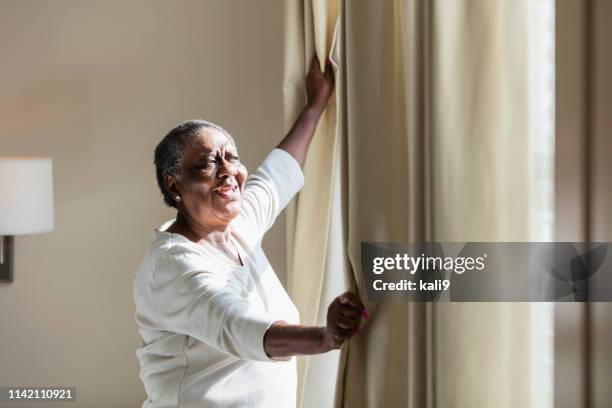 senior african-american woman opening curtain - black curtain stock pictures, royalty-free photos & images