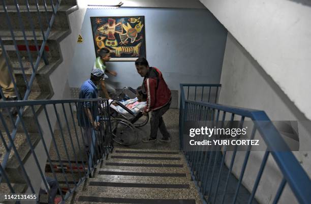 Patient suffering from renal failure is carried up the stairs in a wheelchair to receive hemodialysis treatment at a clinic in Barquisimeto,...