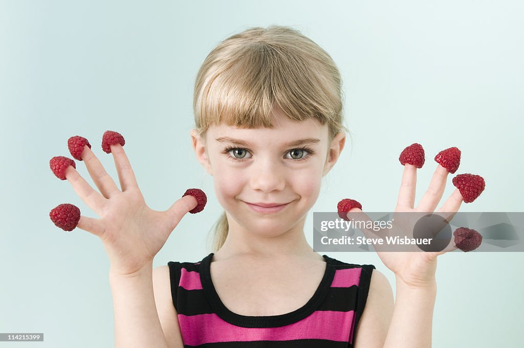 Girl (3-5) with raspberries on fingers, smiling