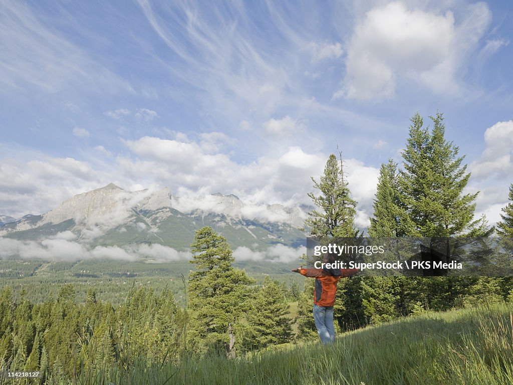 Canada, Alberta, Man standing in mountain meadow with arms outstretched