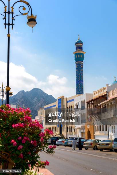 al bahri road im muscat-oman mit blumen und einem walkong seniorenpaar. masjid al rasool moschee - oman skyline stock-fotos und bilder