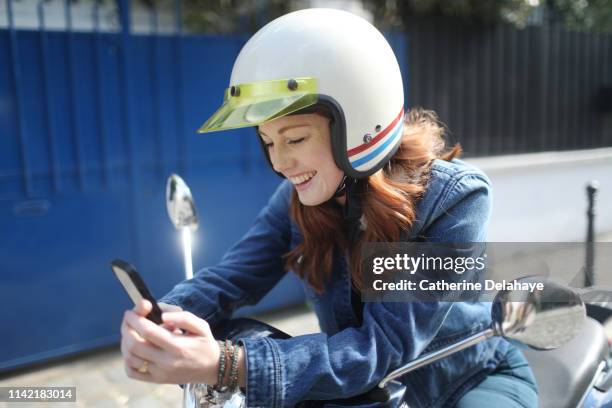 a young woman wearing a helmet, looking at her phone on a scooter in paris - paris street woman stockfoto's en -beelden