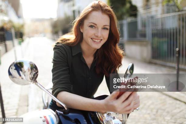 portrait of a young woman sitting on a scooter in paris - beautiful redhead photos et images de collection