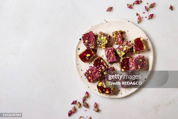 Variety of traditional turkish dessert Turkish Delight different taste and colors with rose petals and pistachio nuts on ceramic plate over white...