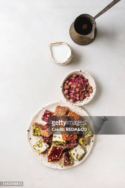 Variety of traditional turkish dessert Turkish Delight with rose petals and pistachio nuts on ceramic plate with coffee jezve and milk jug over grey...