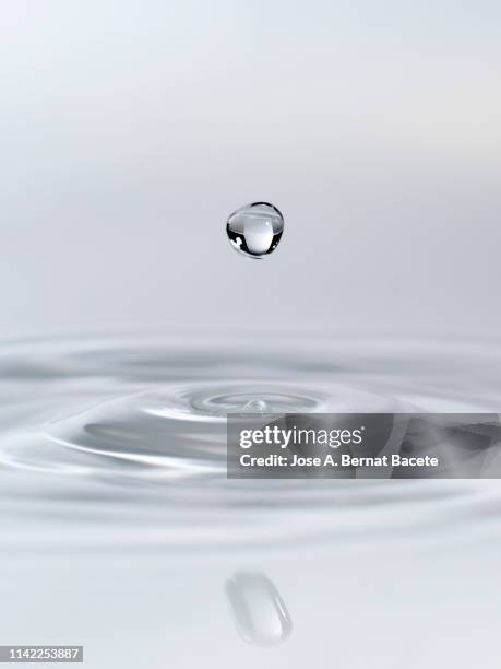 drop suspended in the air, falling down on a water surface that forms figures and abstract forms, on a white background. - splash crown fotografías e imágenes de stock