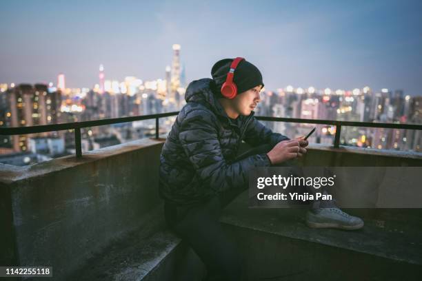 portrait of man using smartphone with headphones on rooftop - ヘッドフォン ストックフォトと画像