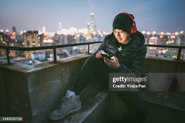 portrait of man using smartphone with headphones on rooftop - shanghai calling stock pictures, royalty-free photos & images